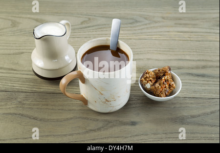 Closeup horizontal photo of a full cup of coffee, snacks and cream in pouring spout with aged wood underneath Stock Photo