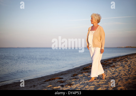 Portrait of a mature woman walking on the beach looking at the sea. Relaxed old lady strolling on the beach with copy space. Stock Photo