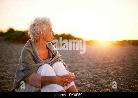Old woman sitting on the beach looking away at copyspace. Senior female sitting outdoors Stock Photo