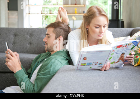 Man Using Smartphone  and Woman Reading Book on Sofa