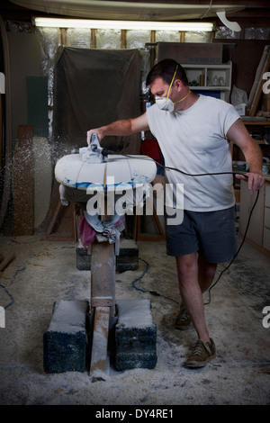 Mature man sanding a surfboard in his garage Stock Photo