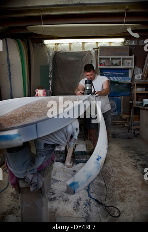 Mature man sawing a surfboard in his workshop Stock Photo