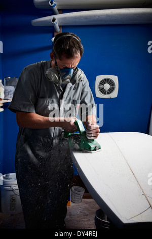 Mid adult man sanding surfboard in his workshop Stock Photo