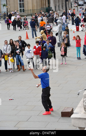 Street Juggler throwing four white balls in the air in front of an audience, Trafalgar Square, London, England, United Kingdom. Stock Photo