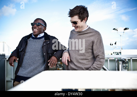 Male friends leaning against fence chatting Stock Photo