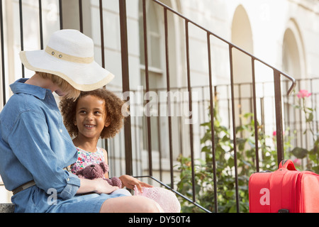 Mother and daughter sitting outside house with suitcase
