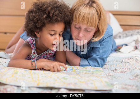Mother and daughter lying on bed, looking at map