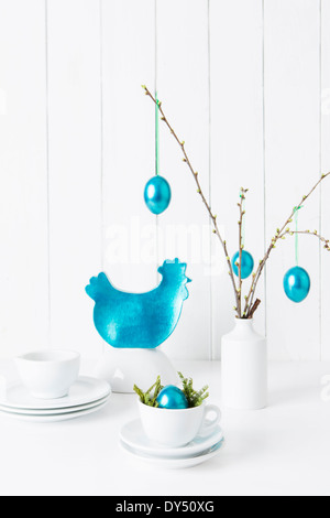 Still life of crockery and turquoise easter eggs hanging from twigs Stock Photo