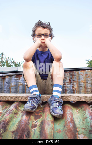 Glum little boy sitting on roof Stock Photo