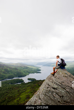 hillwalker sitting on a rock at the top of Ben A'An, in Scotland, looking down at Loch Katrine Stock Photo