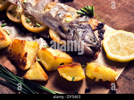 Prepared fish stuffed with lemon and baked potato.Selective focus on the fish head  Stock Photo