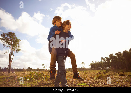 Twin brothers playing piggy back in forest clearing Stock Photo