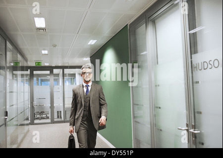 Confident mature businessman walking along office corridor Stock Photo