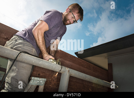 Builder on ladder sawing metal piping Stock Photo