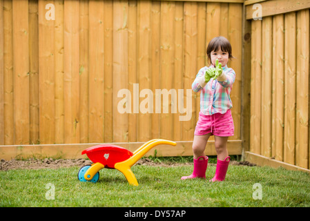 Young girl with toy wheelbarrow putting on gardening gloves