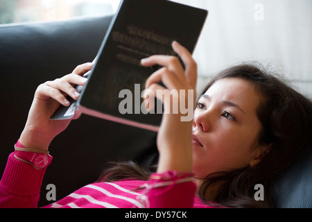 Girl lying on sofa, reading book Stock Photo