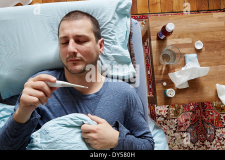 Mid adult man lying in bed looking at thermometer reading Stock Photo