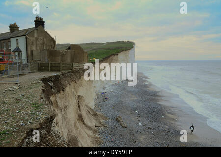 Birling Gap, East Sussex, UK..7 April 2014..Remains of cottage no3 perched on the cliff edge. Rockfalls continue. Surfer walks back along the beach, bottom right, after taking advantage of the waves.David Burr/Alamy Live News
