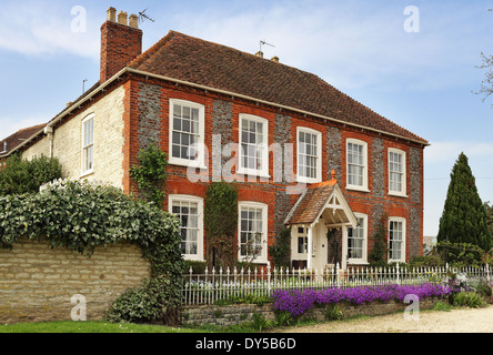 Brick and Flint English Manor Farmhouse with display of purple Aubrietia in front Stock Photo