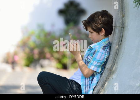 Boy leaning against curved wall texting on cellphone Stock Photo