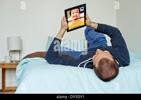 Mid adult man lying on bed holding up digital tablet
