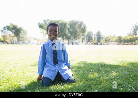 Portrait of boy kneeling on grass in sunlit park Stock Photo
