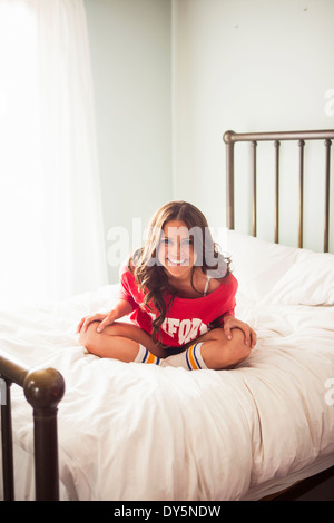 Young woman sitting on bed with legs crossed Stock Photo