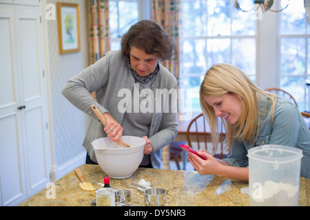 Senior woman and granddaughter baking and using cellphone