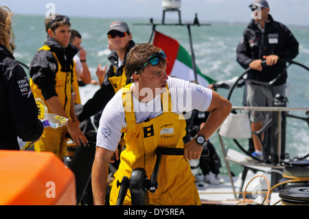 Crewman winch grinding aboard ocean racing yacht, with the skipper on the  wheel behind Stock Photo