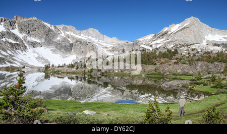 Hiker looks at peaks reflected in lake at 20 Lakes Basin in the Eastern Sierra in Northern California Stock Photo