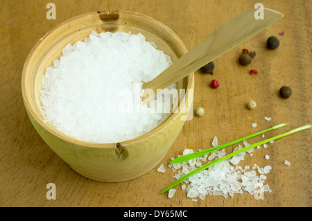 Large sea salt in a wooden bowl with a spoon. On the background of pepper, spices and herbs. Stock Photo
