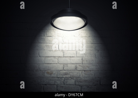 White brick wall illuminated with spot light from the ceiling lamp. Dark interior as background with copy space. Stock Photo