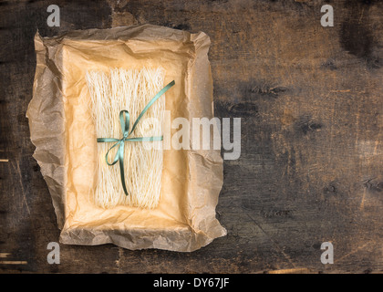 Chinese rice noodles in crumpled paper packaging with green ribbon on an old wooden table Stock Photo