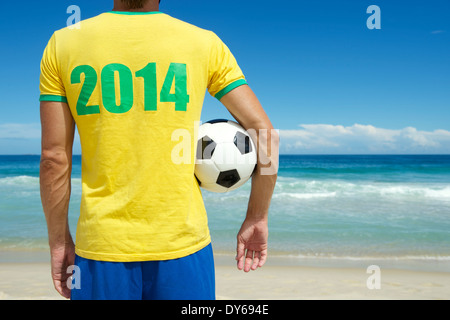 Brazilian soccer player in Brazil colors 2014 shirt holding football tropical beach Stock Photo