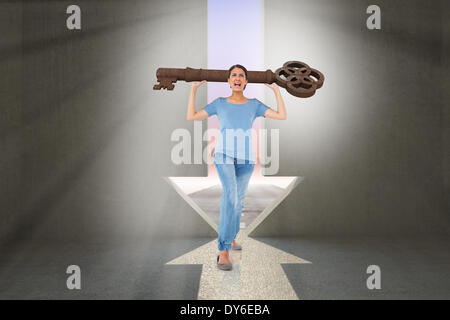 Composite image of annoyed brunette carrying large key Stock Photo