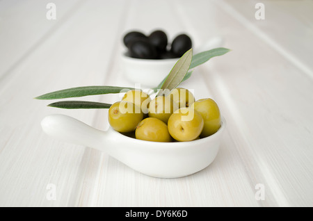 a bowl of green olives in the foreground and the background blurred bowl of black olives on white table Stock Photo