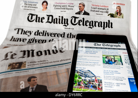 Tablet with  online international news on top of British The Daily Telegraph and French Le Monde newspapers on white background Stock Photo