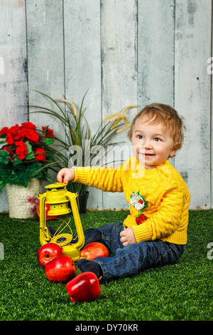 Little boy sits on a lawn in the backyard and at his feet lay ripe apples Stock Photo