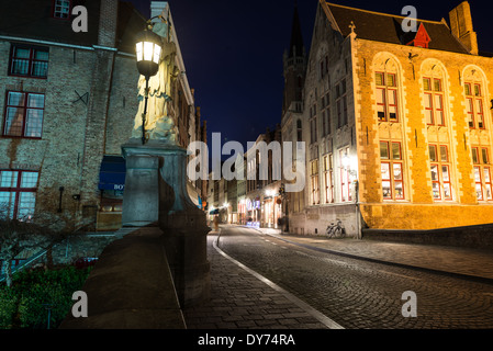 BRUGES, Belgium — A nighttime view from a canal bridge captures the illuminated streets of Bruges' historic center. Traditional lighting reflects off the calm waters, creating a romantic atmosphere characteristic of medieval Bruges after dark. The scene demonstrates how evening illumination enhances the historic character of this UNESCO World Heritage site. Stock Photo