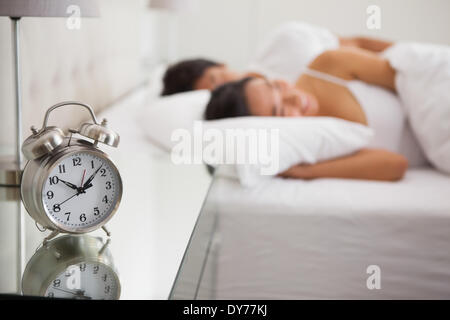 Couple lying in bed with focus on alarm clock
