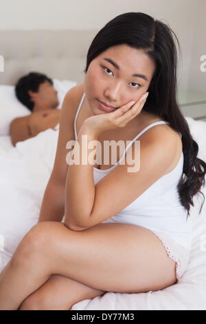 Woman sitting on end of bed as boyfriend sleeps Stock Photo