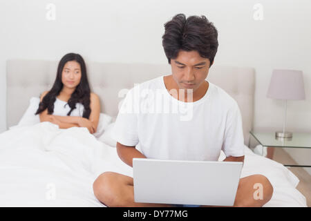 Woman watching boyfriend using laptop on end of bed Stock Photo