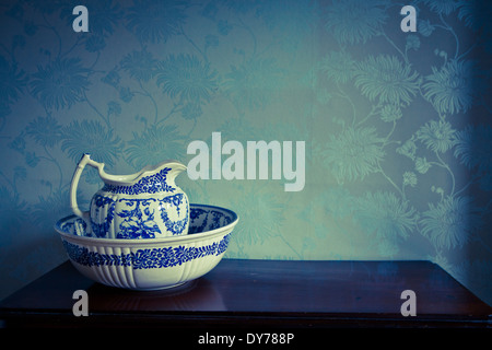 Blue and white Victorian pitcher and wash bowl with blue wallpaper background Stock Photo