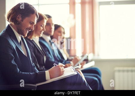 Row of business people making notes at seminar with young man on foreground Stock Photo