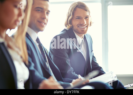 Row of business people sitting at seminar with focus on smiling young man Stock Photo