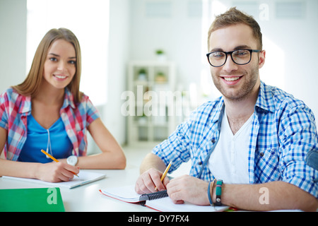Handsome student and his groupmate on background looking at camera while carrying out test at lesson Stock Photo