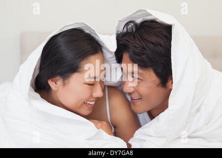 Happy couple lying on bed together under the duvet Stock Photo