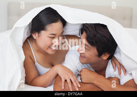 Happy couple lying on bed together under the duvet Stock Photo