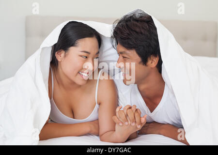 Happy couple lying on bed together under the duvet Stock Photo