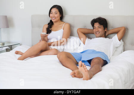 Happy couple lying on bed together watching tv Stock Photo
